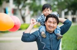 Man with child on shoulder's carrying balloons