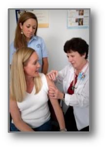 2006 photo of nurse administering a vaccination into the left shoulder muscle of a woman with her family member observing.